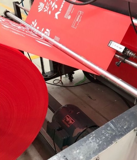 Rollo de tela no tejida roja pasando por una máquina que imprime bolsas ecológicas